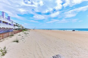 A beach with a wooden fence, a row of buildings with balconies, and a clear sky.