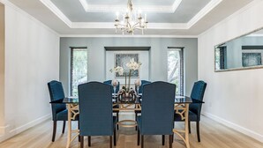 Comedor con mesa de vidrio, sillas azules, lámpara de araña y un espejo grande en la pared.