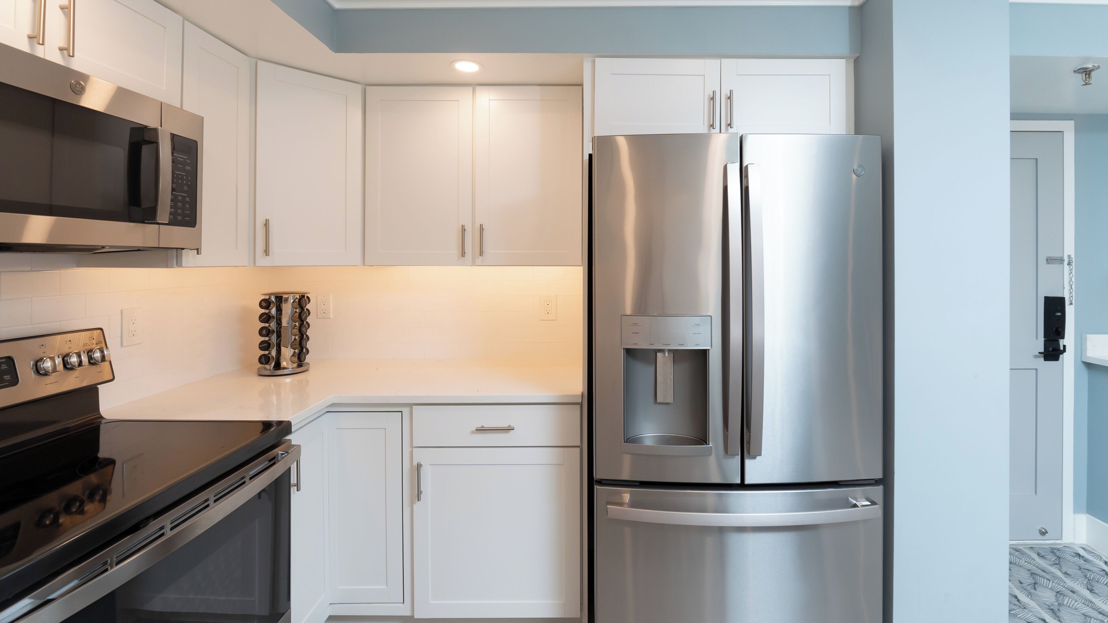 A modern kitchen with white cabinets, stainless steel appliances including a refrigerator and oven, and a built-in water dispenser.