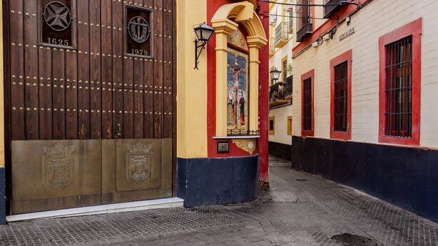 Una calle estrecha con una puerta de madera marcada '1625' y '1979', un edificio colorido con un mural y un letrero que dice 'DESCAT ZOS'.