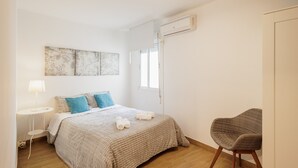 Un dormitorio con cama, una silla, una lámpara y obras de arte en la pared.