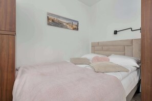 Un dormitorio con cama, cabecera, lámpara de pared y un cuadro.