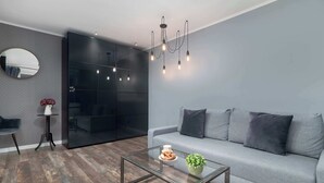 Una sala de estar moderna con un sofá gris, una mesa de centro de vidrio, un espejo redondo y un armario negro.