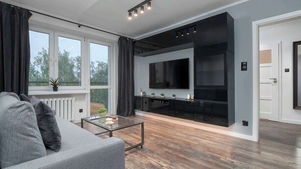 Una sala de estar moderna con un sofá gris, una mesa de centro de vidrio y un televisor de pantalla plana grande montado en la pared.