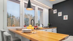 Una cocina moderna con encimera de madera, una lámpara colgante negra y vistas a árboles.
