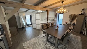 A spacious living area with a large dining table, a comfortable sofa, and a chandelier.