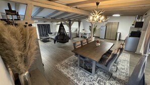 Een ruime woonkamer met een houten eettafel, banken en een hangstoel.