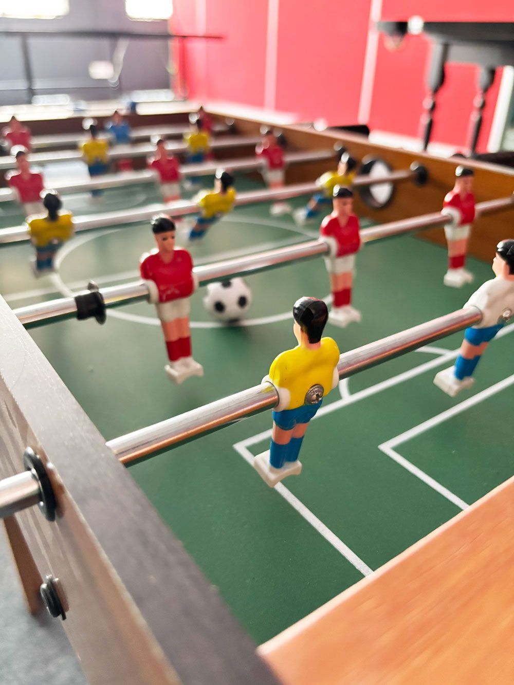 A tabletop foosball table with miniature soccer players in red and yellow uniforms.