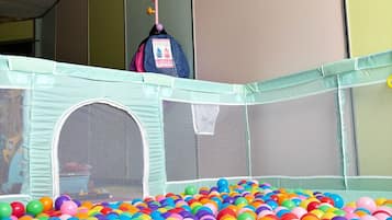 Een bällebak vol kleurrijke plastic ballen, een veiligheidshek en een roze en blauwe tas hangend aan een paal.