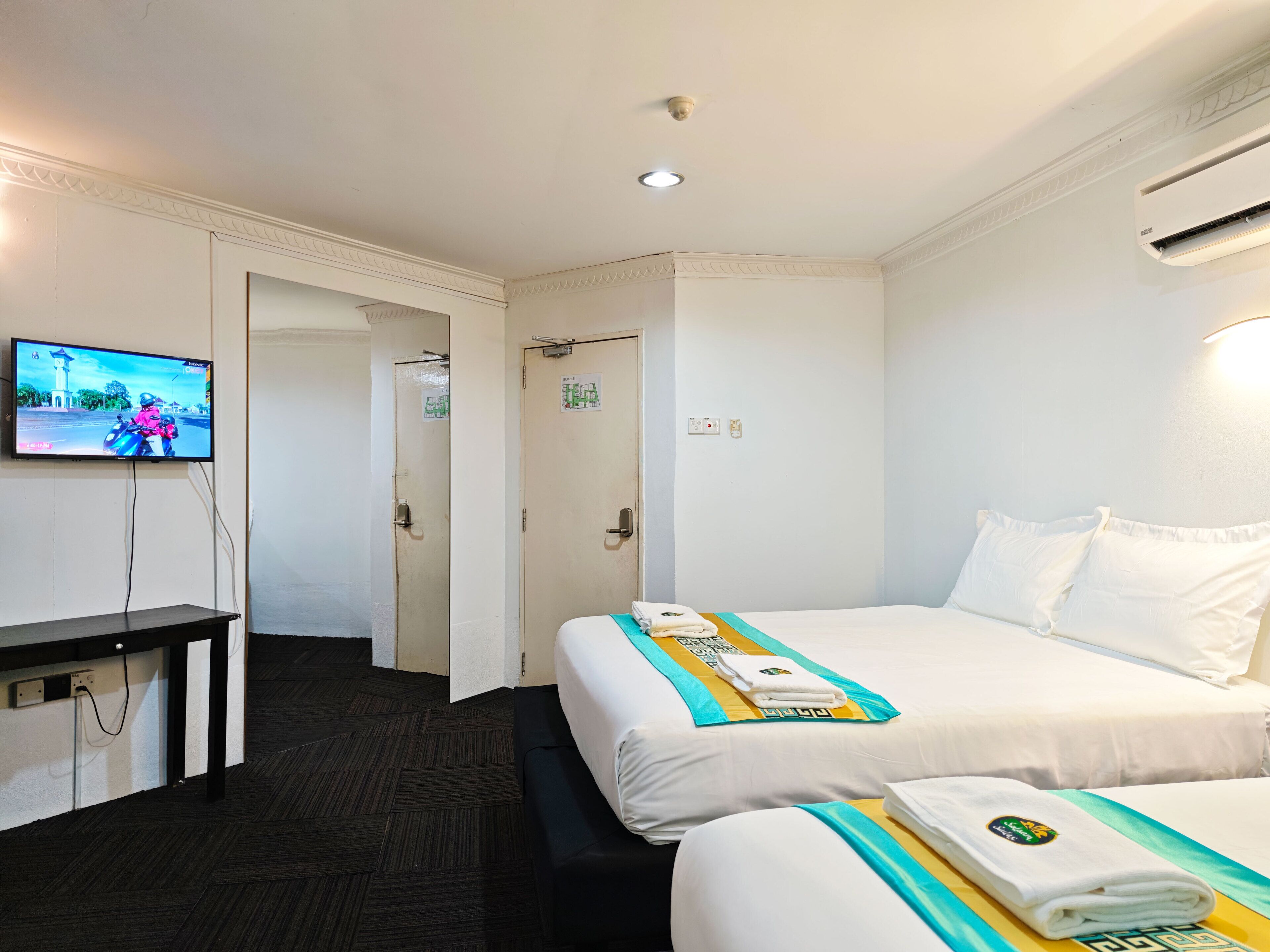 A hotel room with a bed, a TV, a desk, and a bathroom door.
