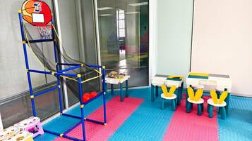 A play area with a basketball hoop, small tables, and colorful play mats.