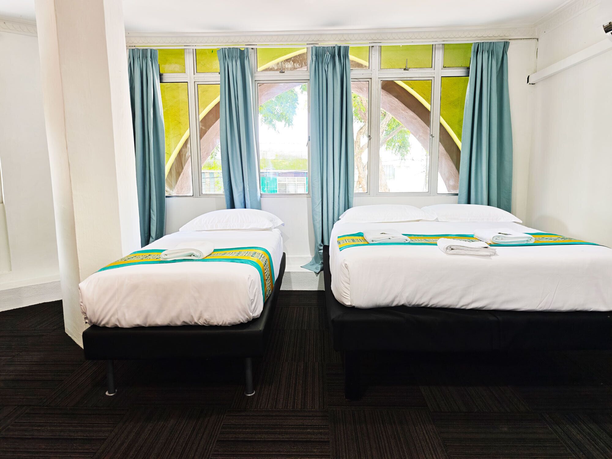 Habitación de hotel con dos camas individuales, una ventana con cortinas y vistas a zonas verdes.