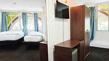 Habitación de hotel con dos camas, un televisor montado en la pared, un armario de madera y un refrigerador pequeño.