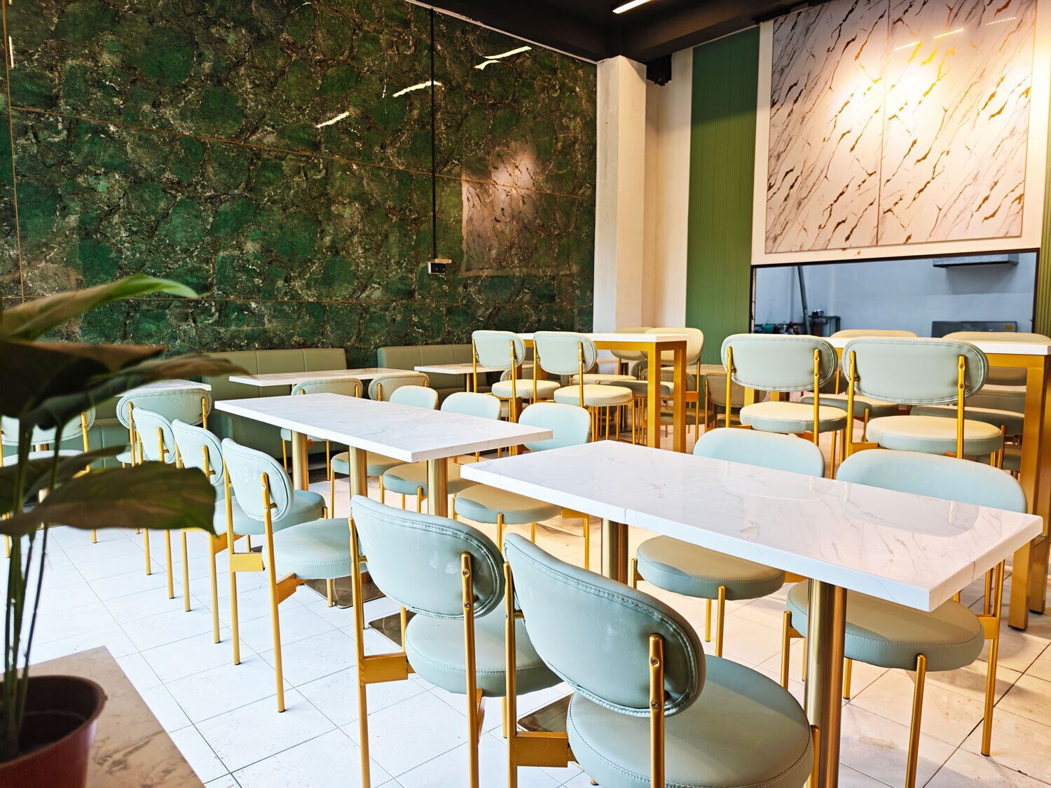 A modern restaurant interior with marble tables and green upholstered chairs.