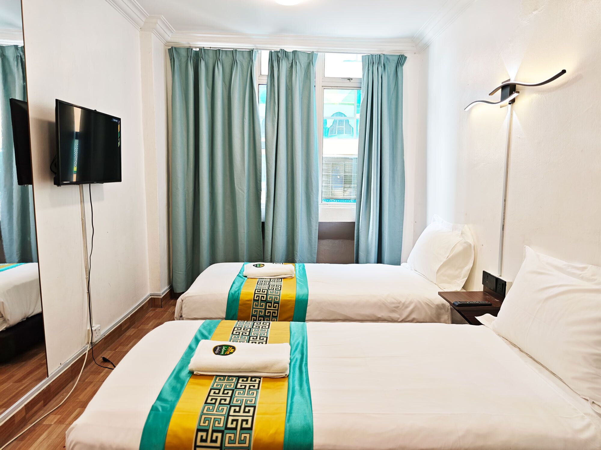 Een hotelkamer met twee bedden, een televisie en een raam met gordijnen.