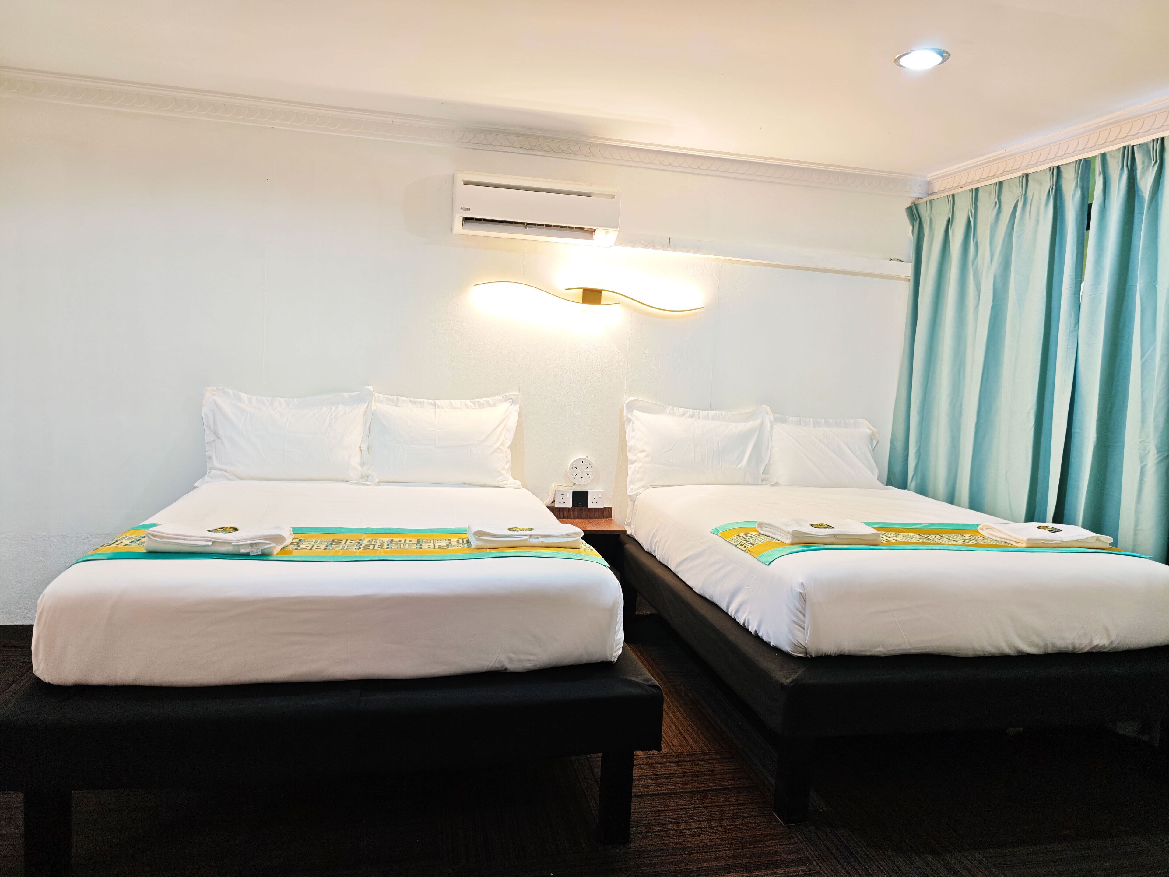 Habitación de hotel con dos camas, una mesita de noche, un equipo de aire acondicionado y una ventana con cortinas.