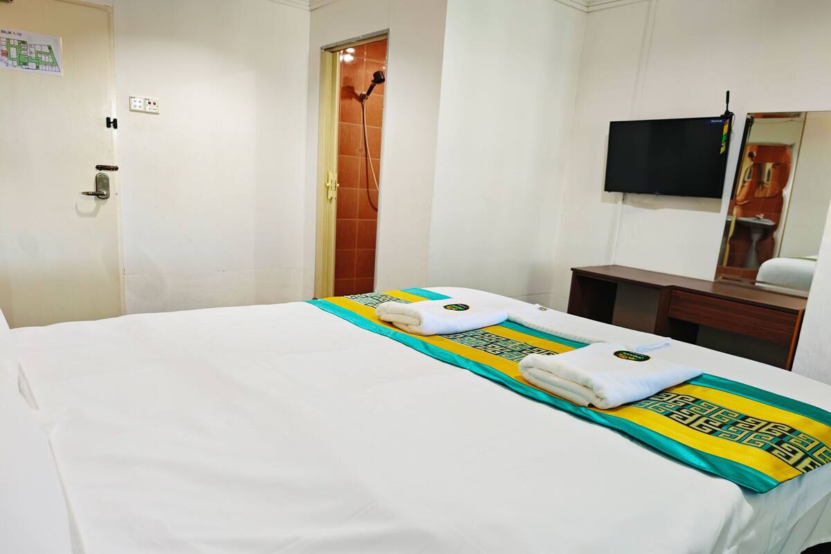 Quarto de hotel com uma cama, uma televisão presa à parede e uma porta com um mapa.