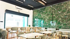 Un área de comedor moderna con mesas y sillas, un ventanal grande y una pared de mármol verde.