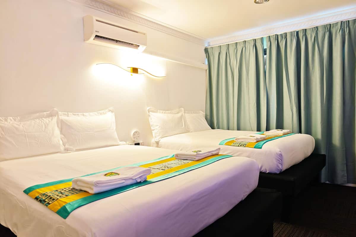Quarto de hotel com duas camas, ar condicionado fixado na parede, mesa de cabeceira com luminária e janela com cortinas.