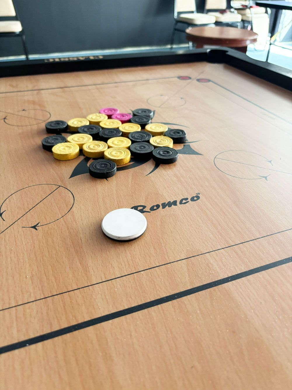 A wooden table with a white puck and multicolored pegs, possibly for a game, with the word "Romco" on it.
