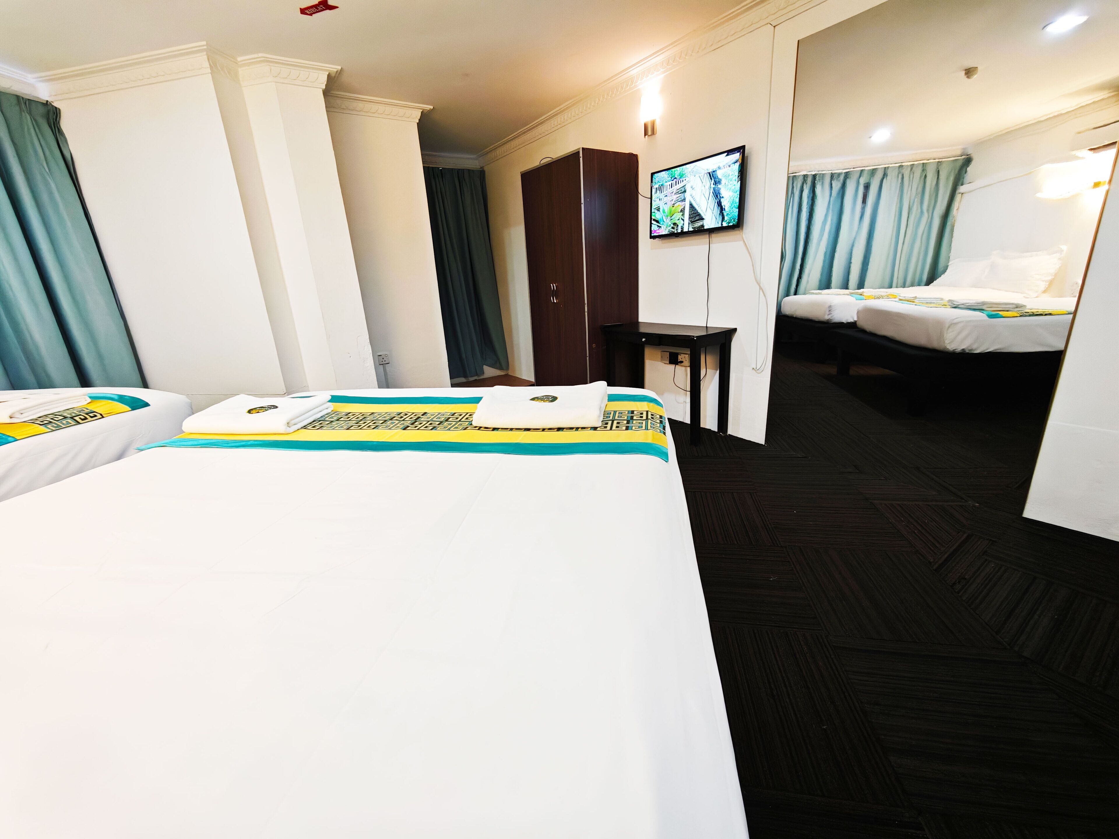 Habitación de hotel con dos camas, un televisor montado en la pared y un escritorio.