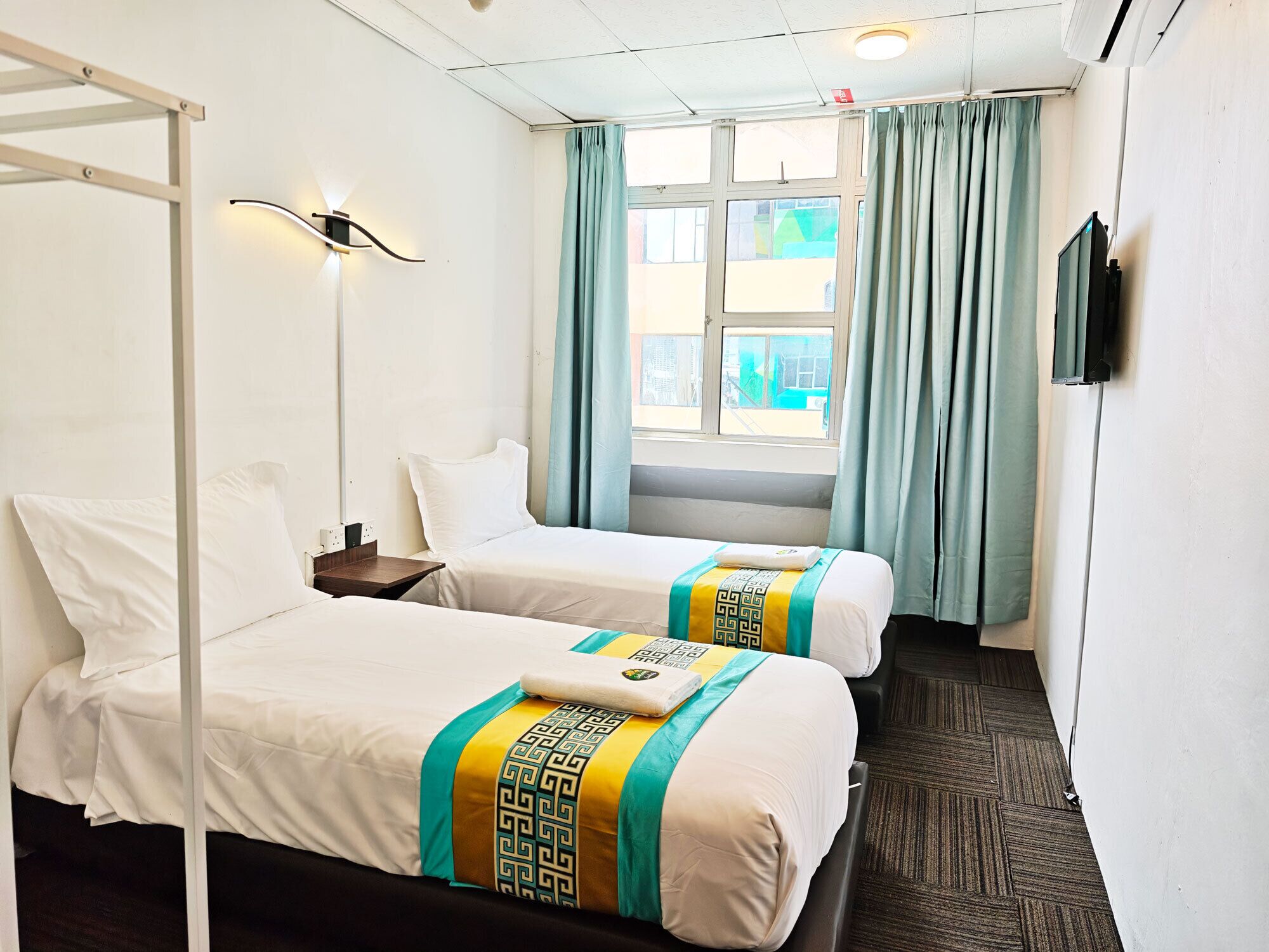 A hotel room with two beds, a window with curtains, a flat-screen TV, and a ceiling fan.