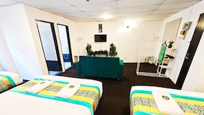 Habitación de hotel con dos camas, televisor, espejo y sofá verde.