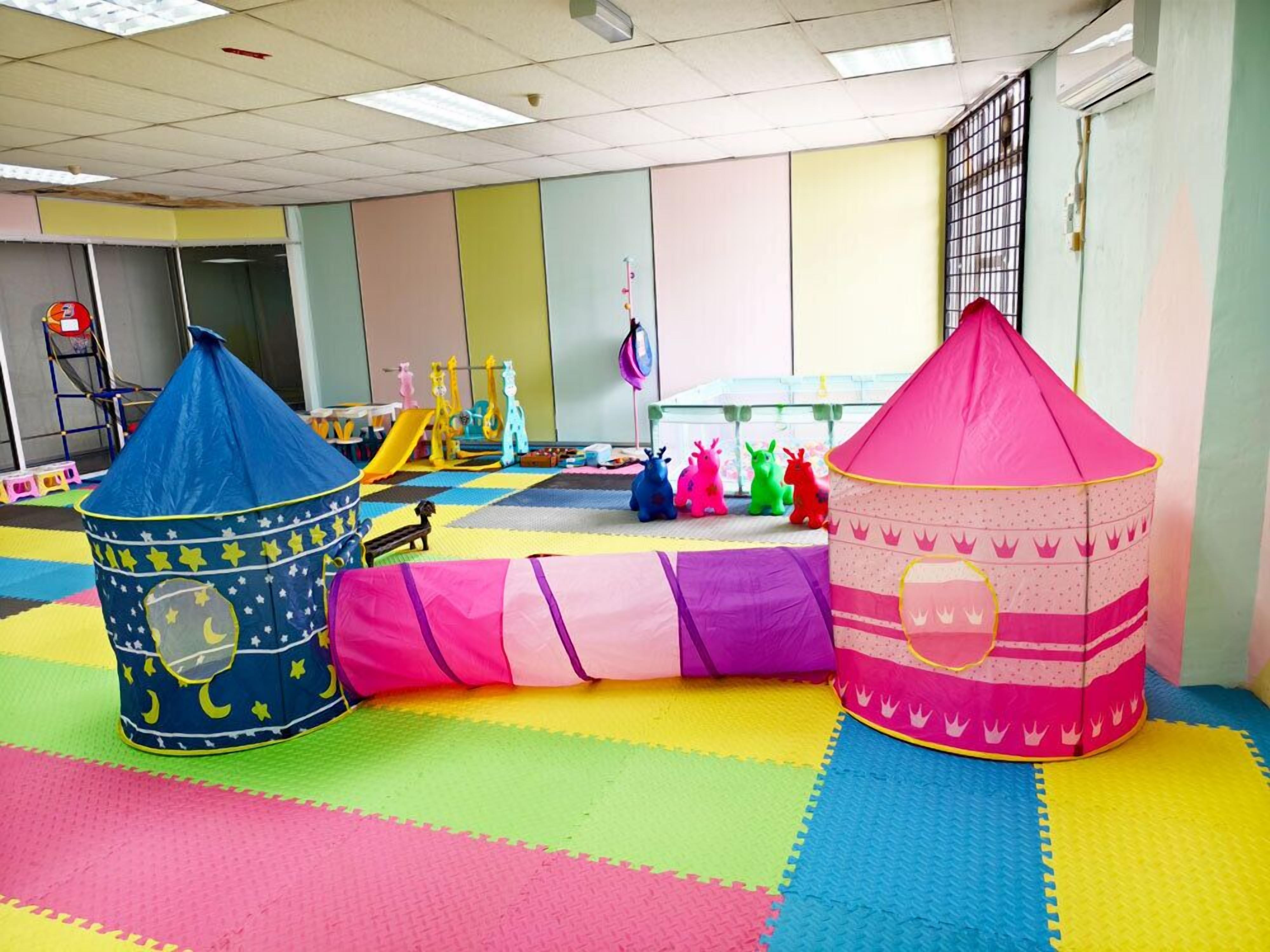 A play area with colorful mats, a blue and pink play tent, and various toys.