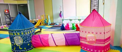 A play area with colorful mats, a blue and pink play tent, and various toys.