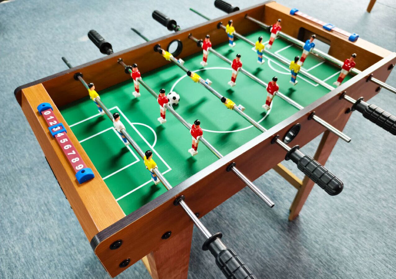 Une table de baby-foot avec de minuscules joueurs de football portant des maillots rouges et jaunes.