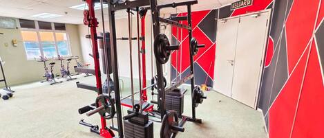 Une salle de sport équipée de matériel de musculation, avec un décor mural aux couleurs rouge et noir, et une fenêtre offrant une vue agréable.