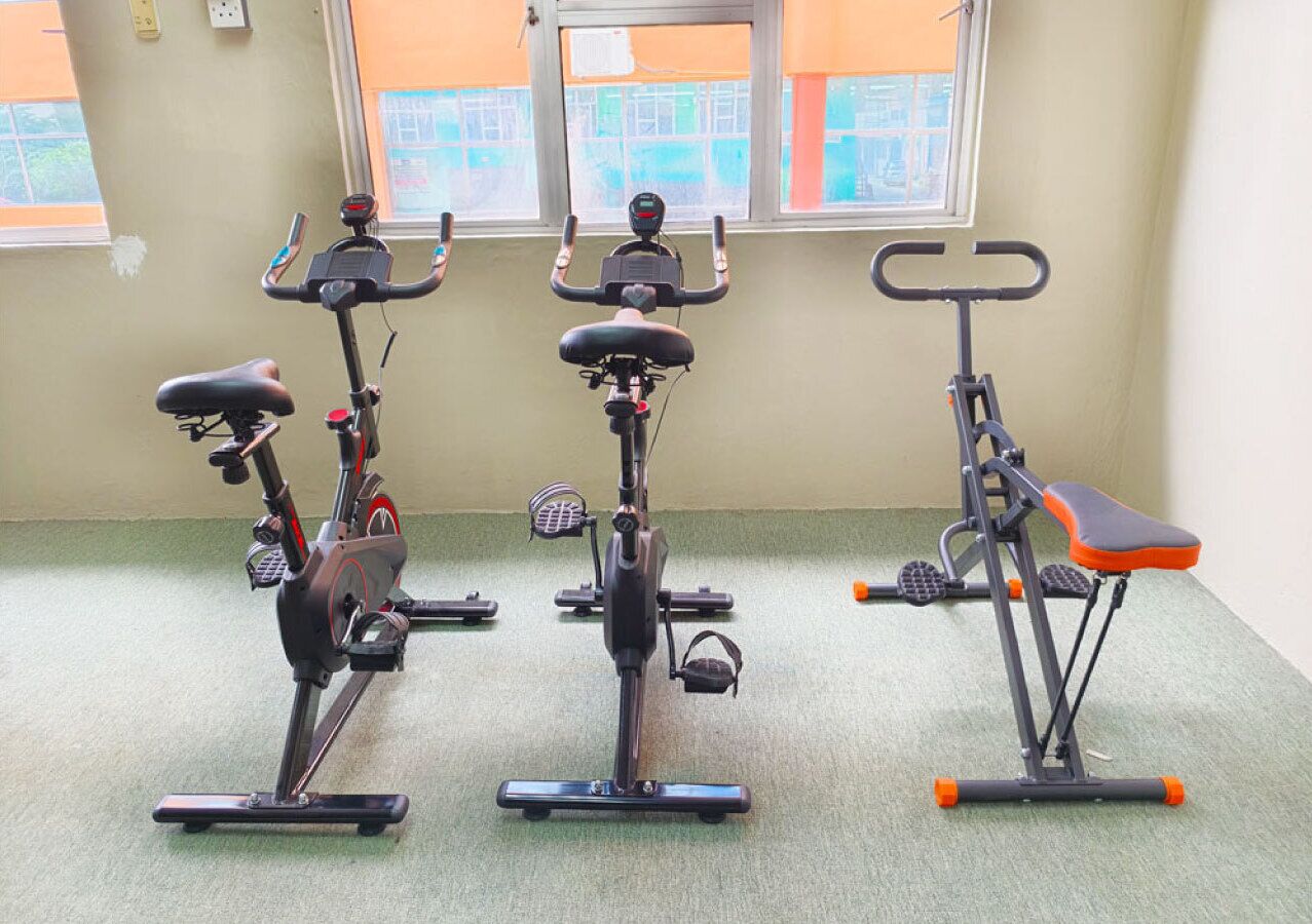 Three stationary bikes in a room with a green carpet and windows with orange blinds.