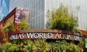 Señal del Acuario Mundial de Dallas con un edificio de cristal grande al fondo.