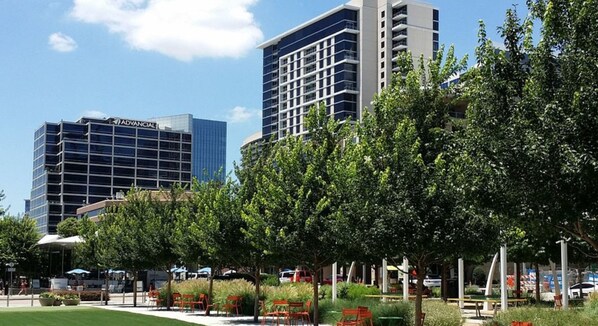 Un edificio moderno con fachada de vidrio, rodeado de jardines y mobiliario exterior.