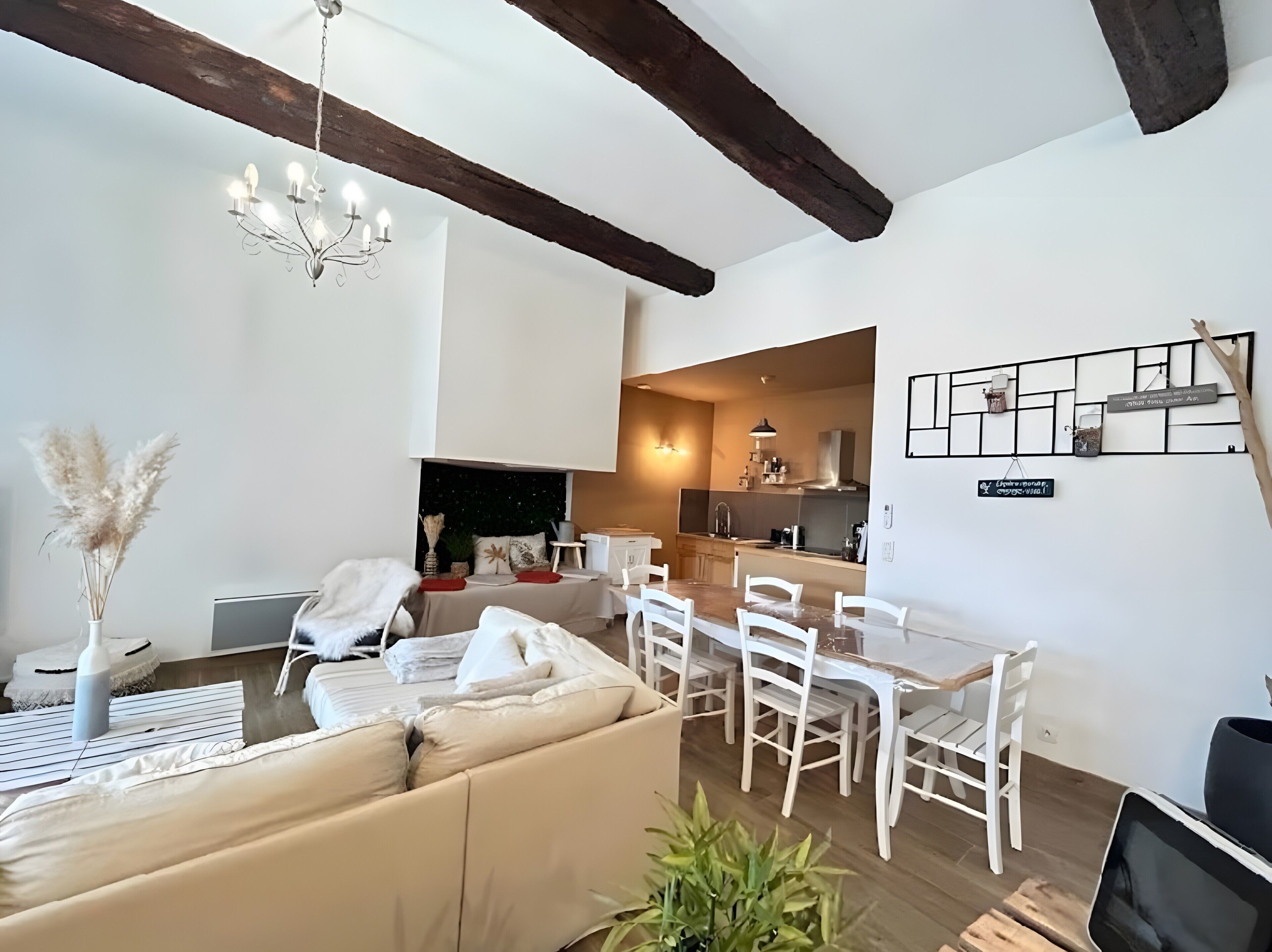 Uma sala de estar moderna com sofá, mesa de jantar e cadeiras, área de cozinha e um candelabro.