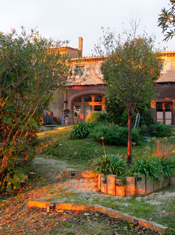 Un jardín con un sendero que lleva a un edificio con techo de tejas y chimenea.