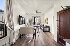 A modern living room with a dining area, a sofa, a TV, and a ceiling fan. - Artifact Inn - Stylish 2BR Gaslamp Suite Top Spot (San Diego)
