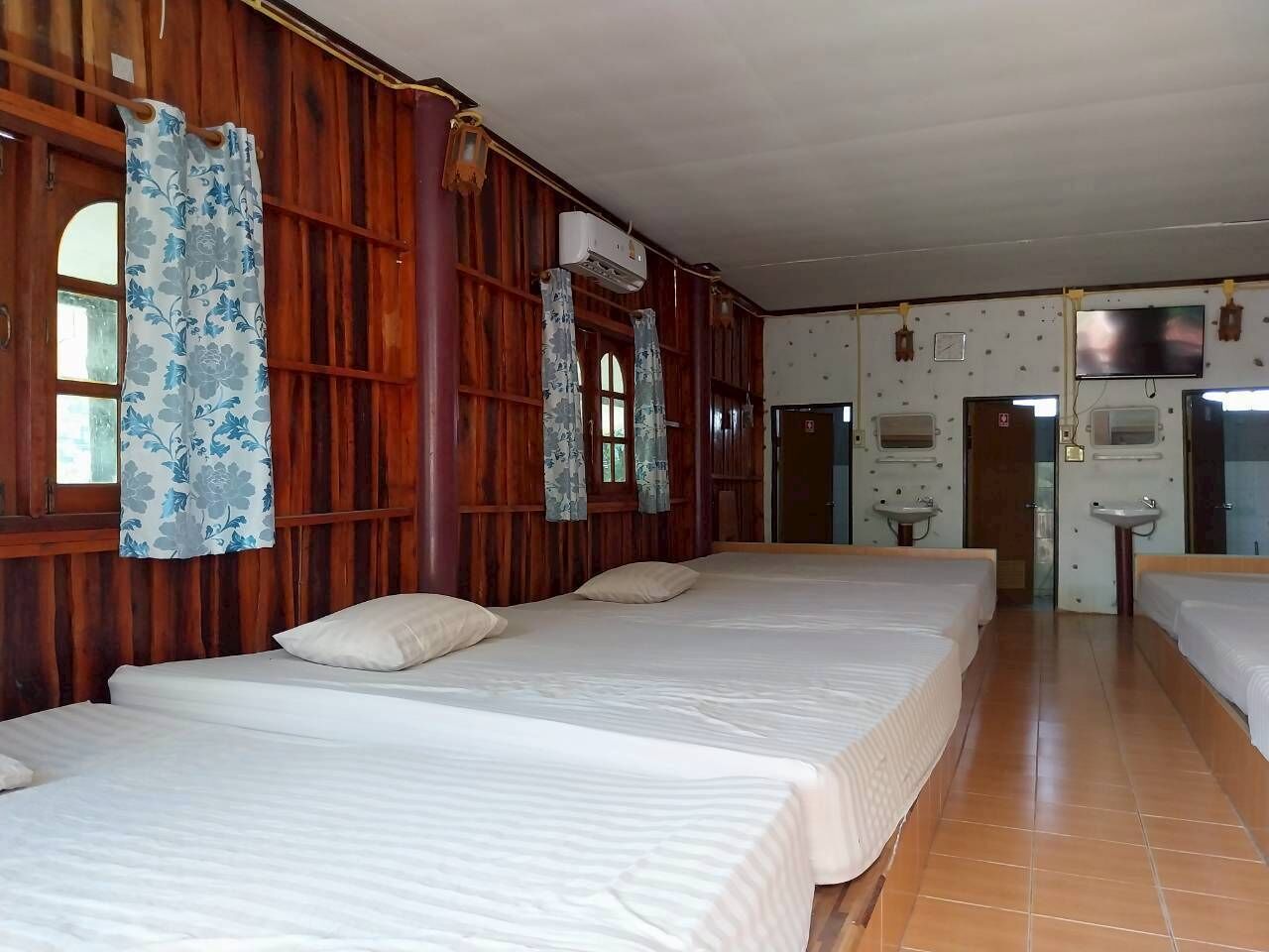 A hotel room with three beds, wooden walls, a large window, and a bathroom with a sink and mirror.