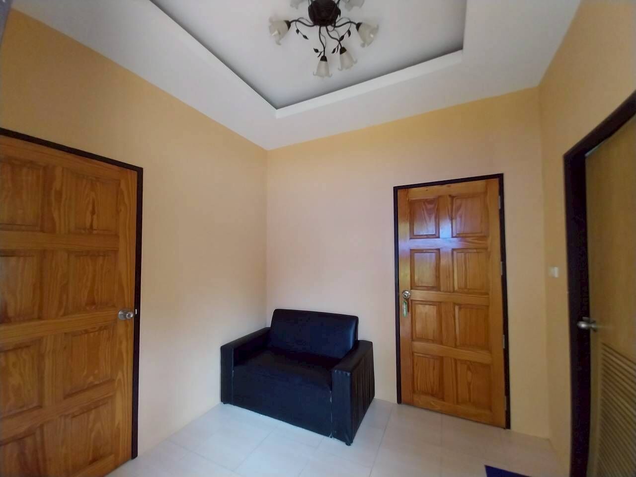 Una habitación con dos puertas de madera, un sofá negro y una lámpara en el techo.
