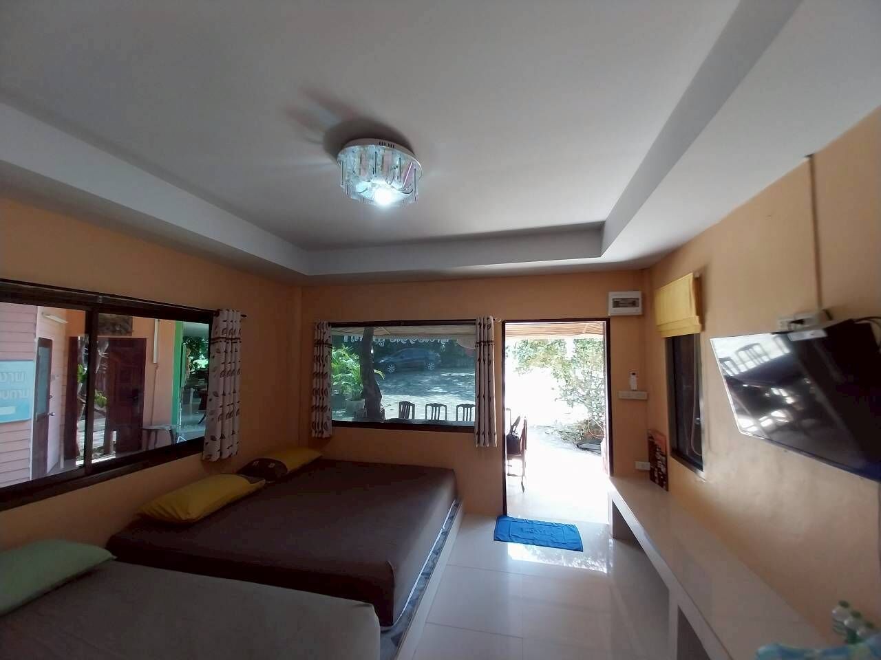A room with two beds, a ceiling fan, a window with curtains, and a TV mounted on the wall.
