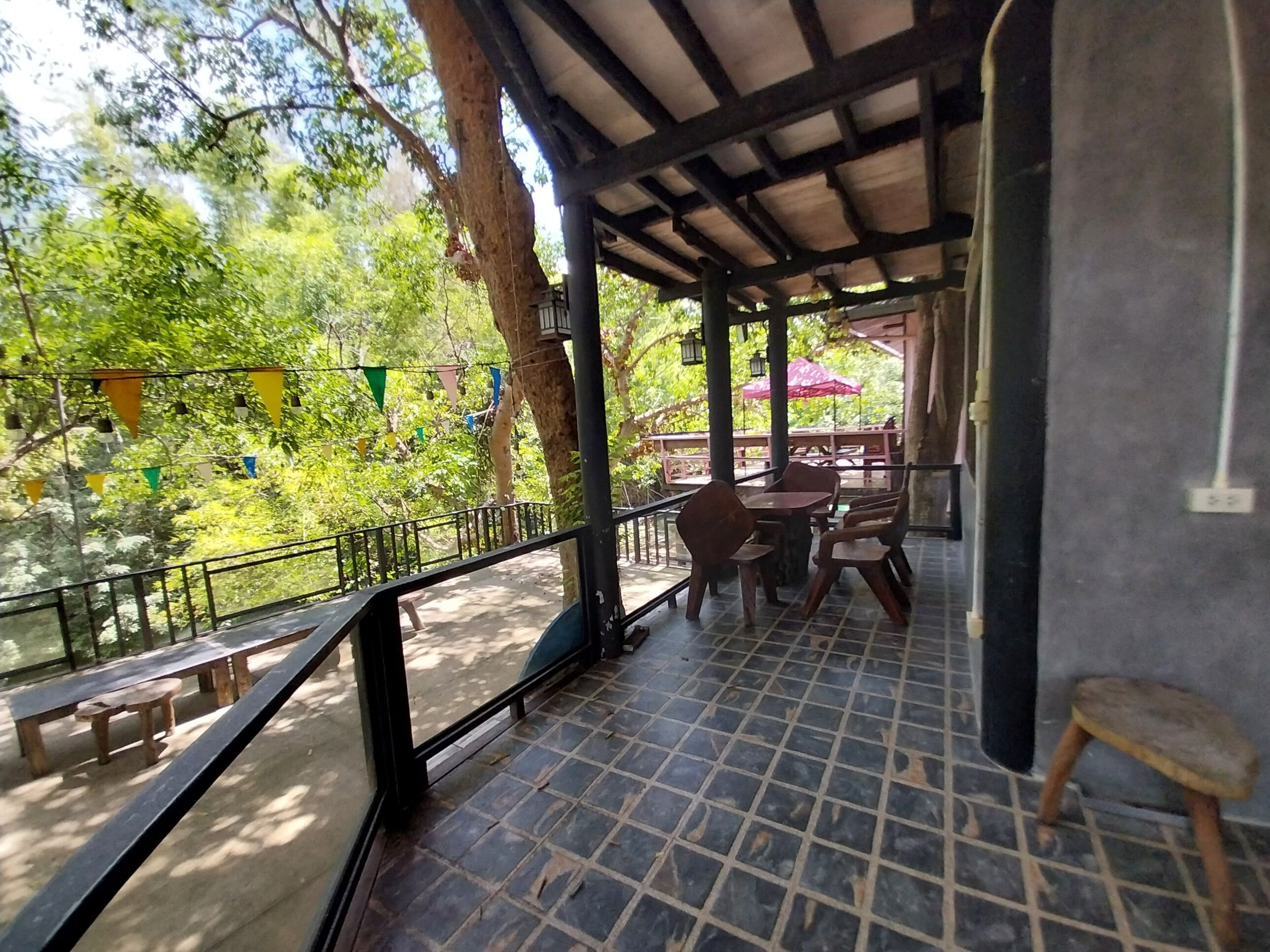 Un espace extérieur abrité, aménagé avec des tables et des chaises, et entouré d’arbres et de verdure.