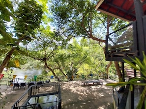 An outdoor seating area with tables and chairs, surrounded by trees and a view of a body of water. - Bamboo River House Kaeng Krachan (Kaeng Krachan)
