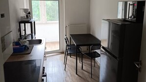 Une cuisine compacte dotée d’un plan de travail noir, d’une cuisinière encastrée, d’un réfrigérateur et d’une table à manger avec des chaises.