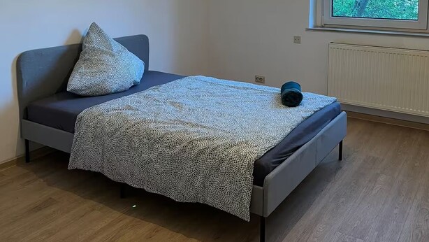 Une chambre à coucher avec un lit, une fenêtre donnant sur des arbres et un luminaire au plafond.