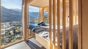 Un dormitorio con una cama y vistas a un paisaje urbano, con montañas al fondo.
