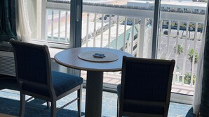 A hotel room with a large window offering a view of the beach and ocean. There is a round table with two chairs and a small rug on the floor. - The Beachline Ocean View Studio Condo (Daytona Beach)