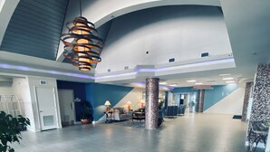 A spacious lobby with a high ceiling, a modern chandelier, and a seating area with tables and chairs. - The Beachline Ocean View Studio Condo (Daytona Beach)