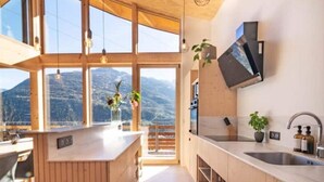 A modern kitchen with wooden cabinetry, a large island, and a view of mountains through large windows.