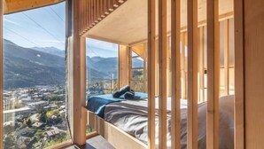 A bedroom with a large window, wooden beams, and a bed.