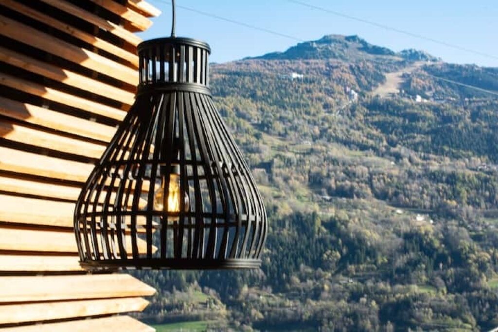 A black metal lantern hanging outdoors with a view of a mountainous landscape in the background.